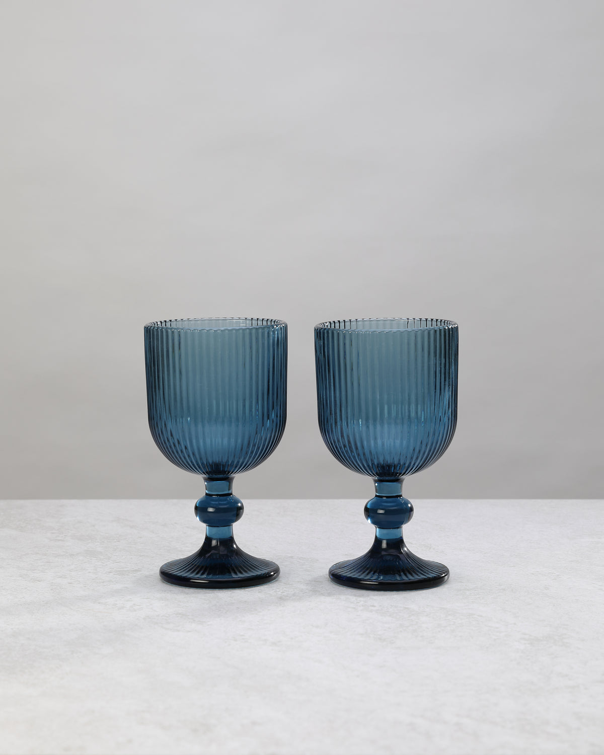 Two blue ribbed wine glasses on short knotted stems, on white