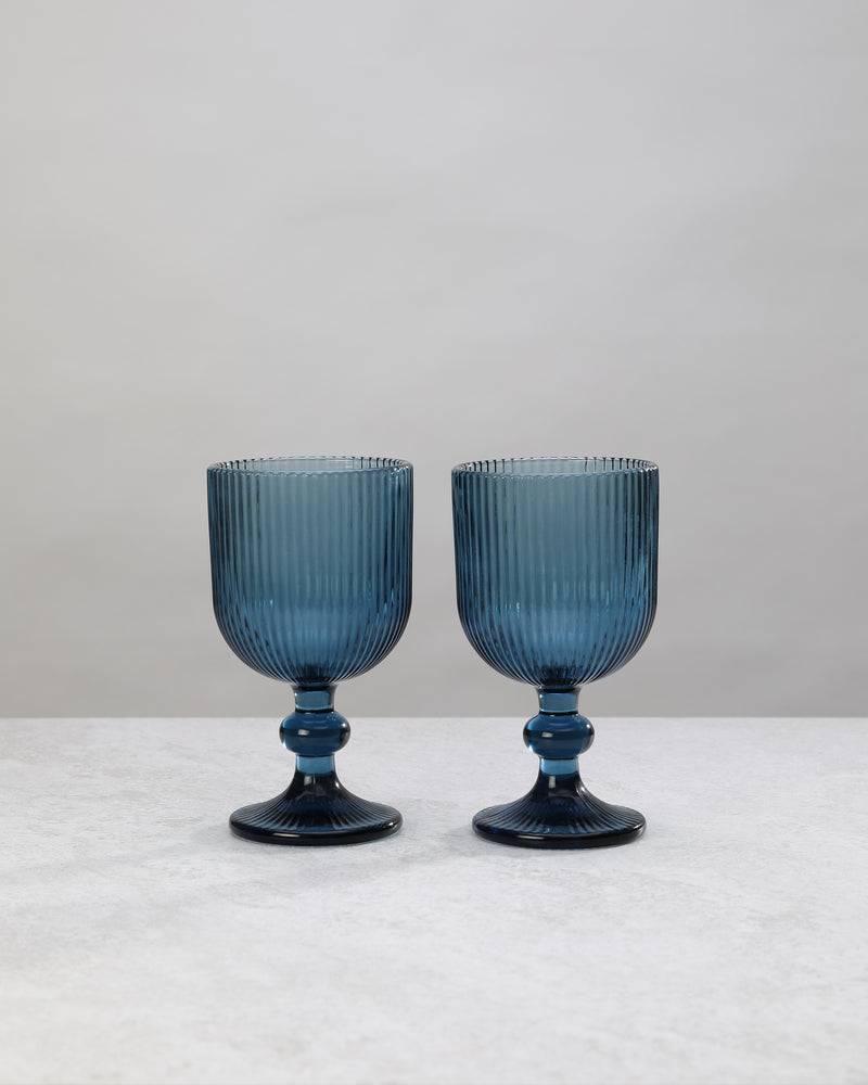 Two blue ribbed wine glasses on short knotted stems, on white