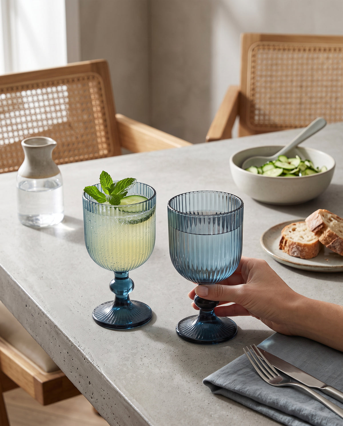 Blue ribbed wine glasses with lemonade and mint at a lunch table, a hand holding one