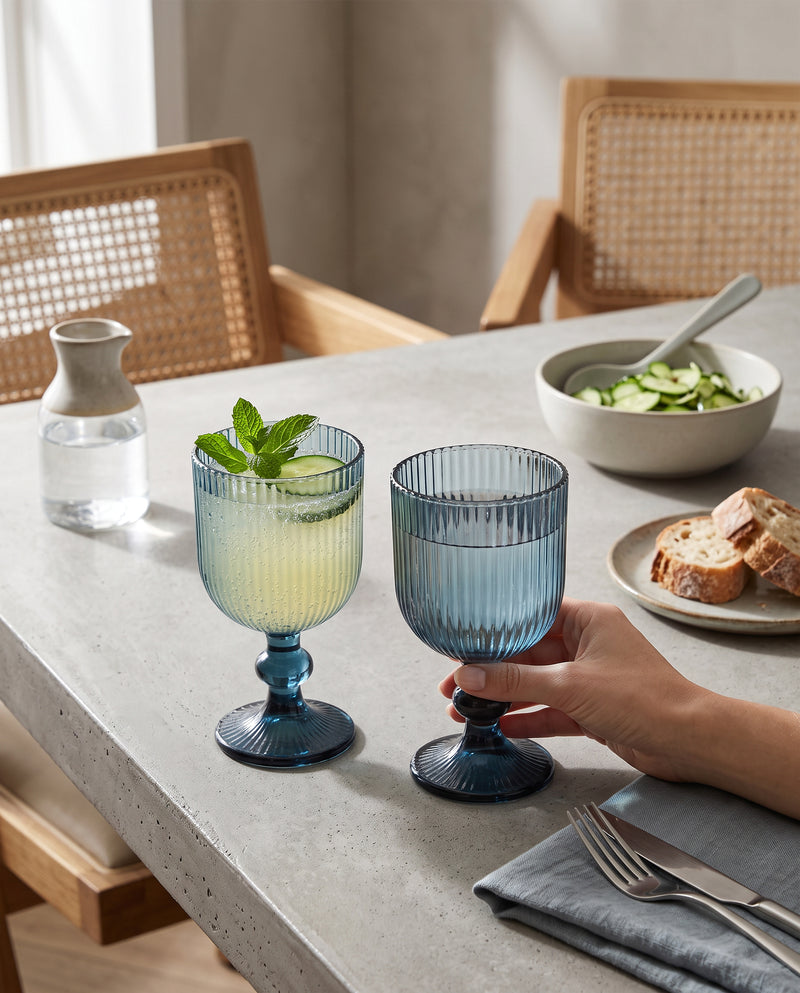 Blue ribbed wine glasses with lemonade and mint at a lunch table, a hand holding one
