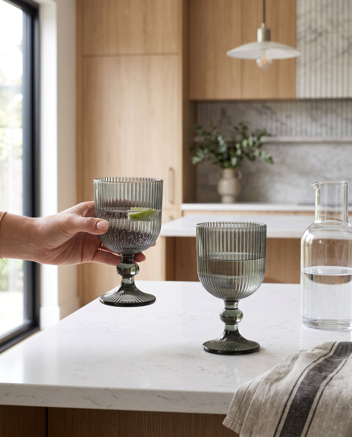 Hand holding a hunter green ribbed wine glass at a kitchen counter