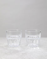 Two clear water glasses with a faceted lower band, on white