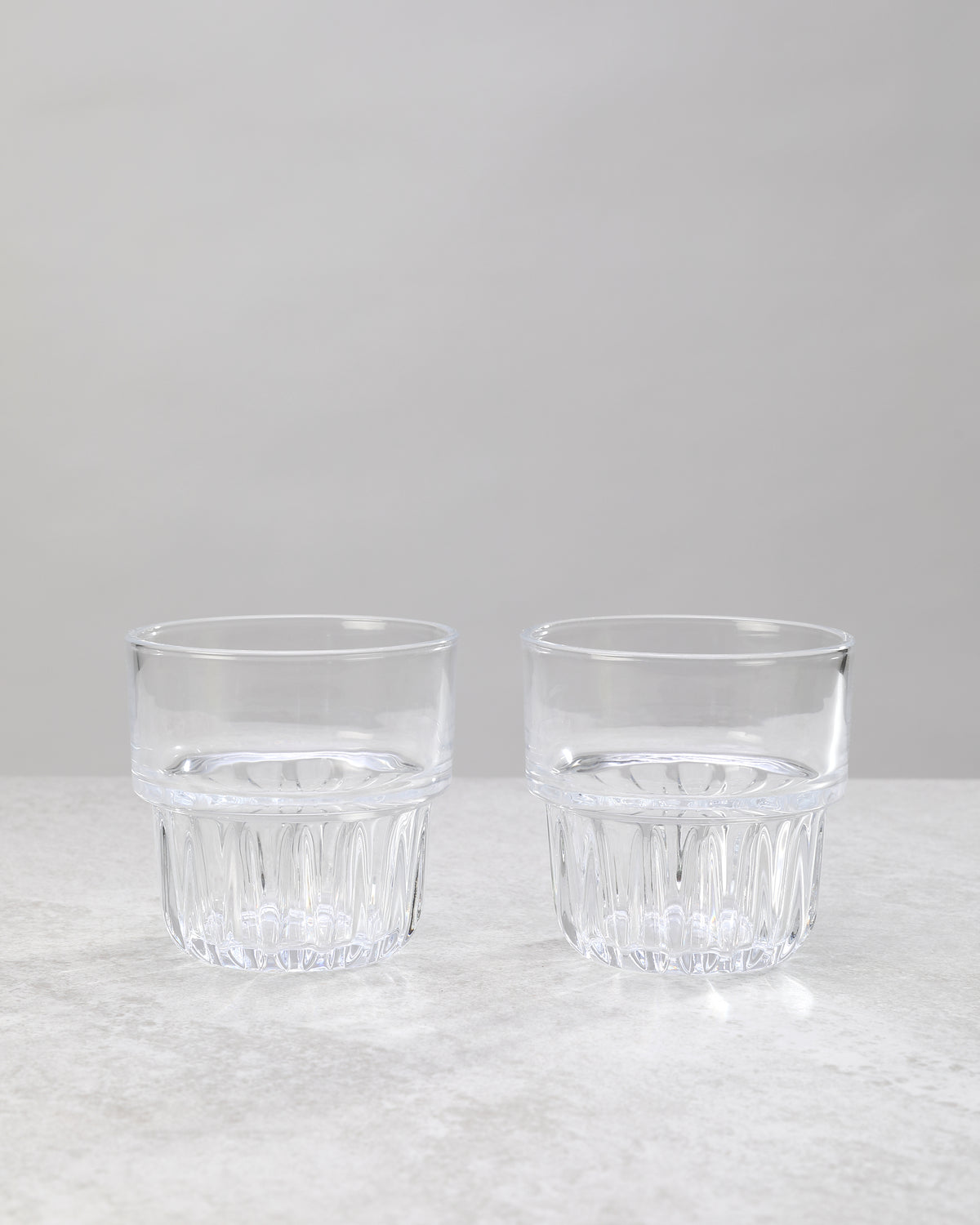 Two clear water glasses with a faceted lower band, on white