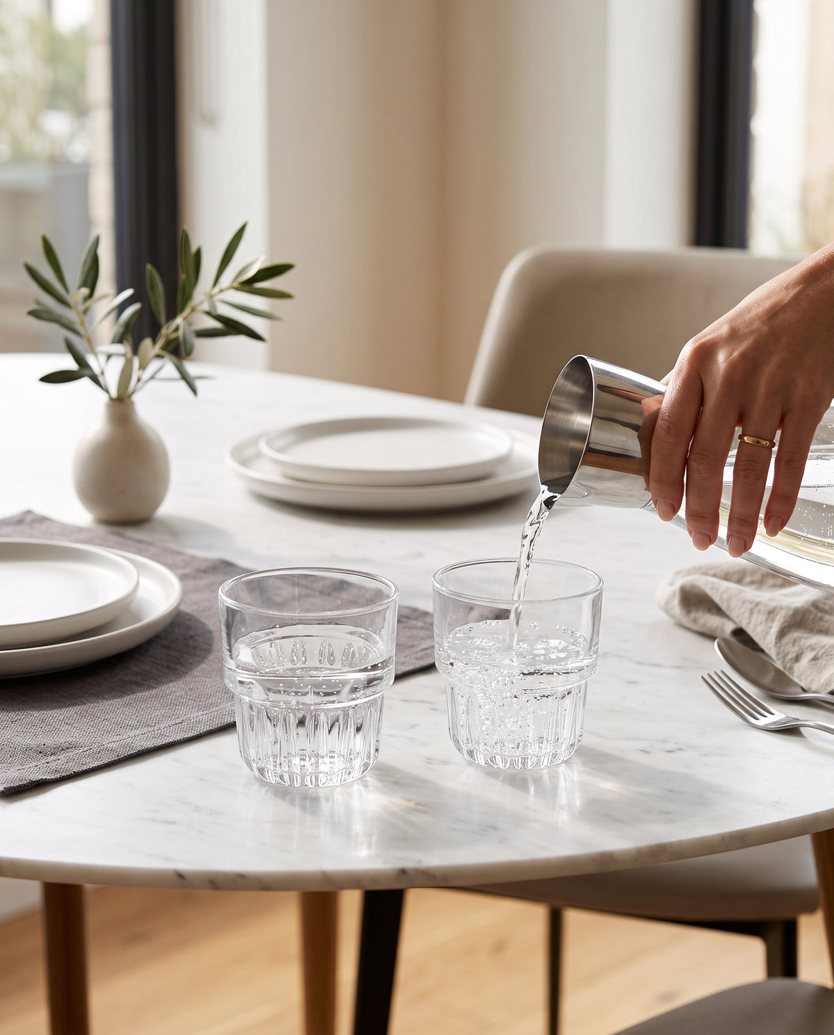 Water being poured into clear glasses on a round marble dining table