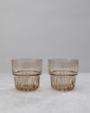 Two amber water glasses with a faceted lower band, on white
