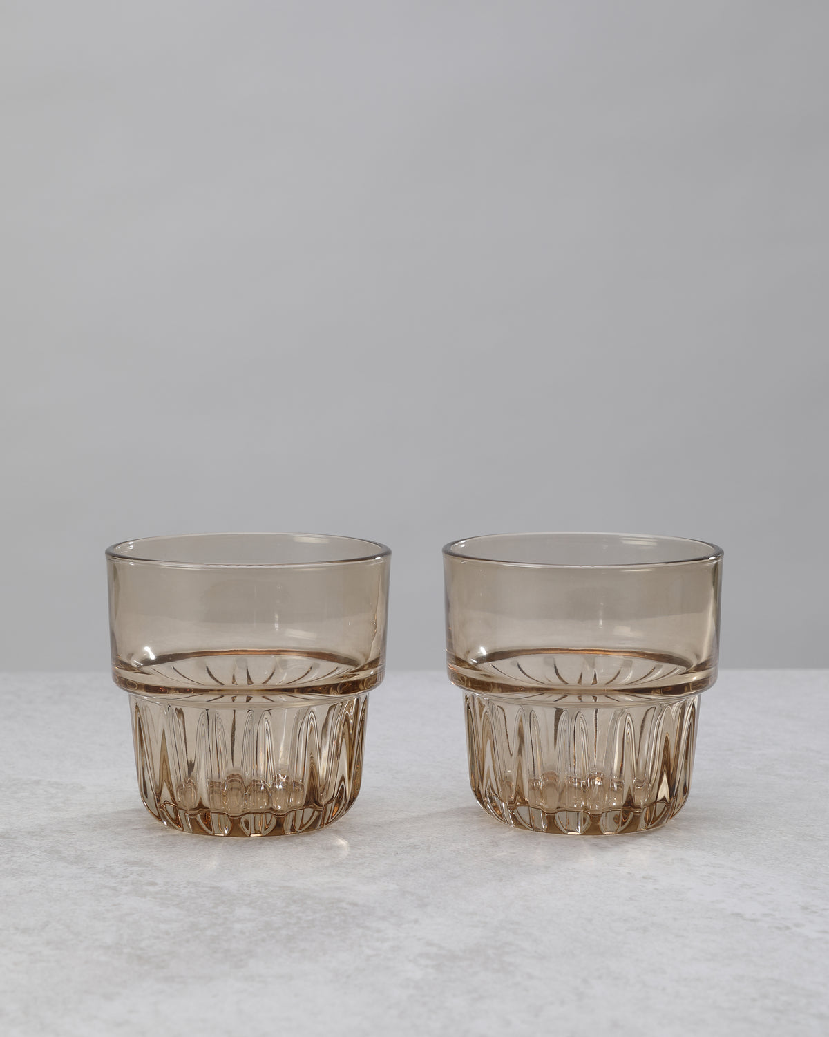 Two amber water glasses with a faceted lower band, on white