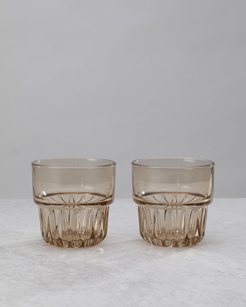 Two amber water glasses with a faceted lower band, on white