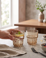 Amber water glasses on a dining table with a slice of lime, a hand lifting one