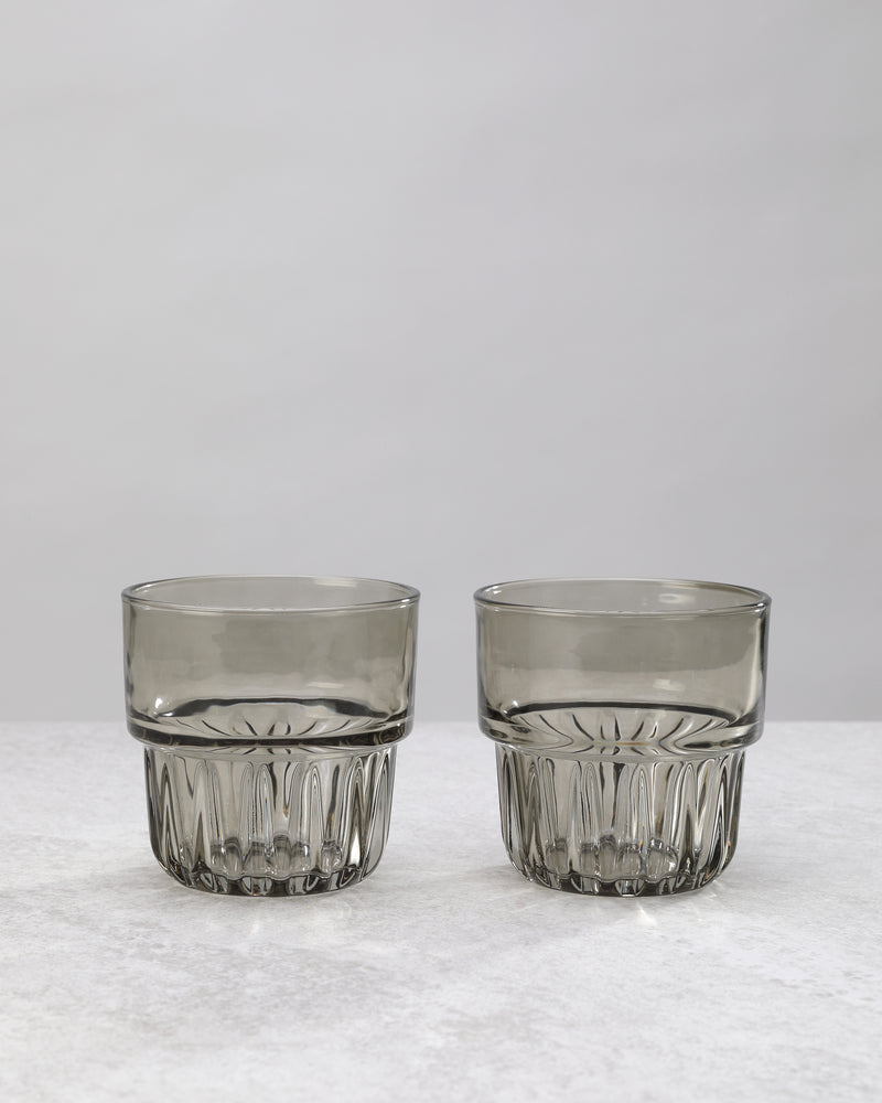 Two grey water glasses with a faceted lower band, on white