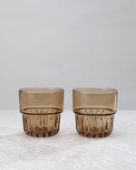 Two brown water glasses with a faceted lower band, on white