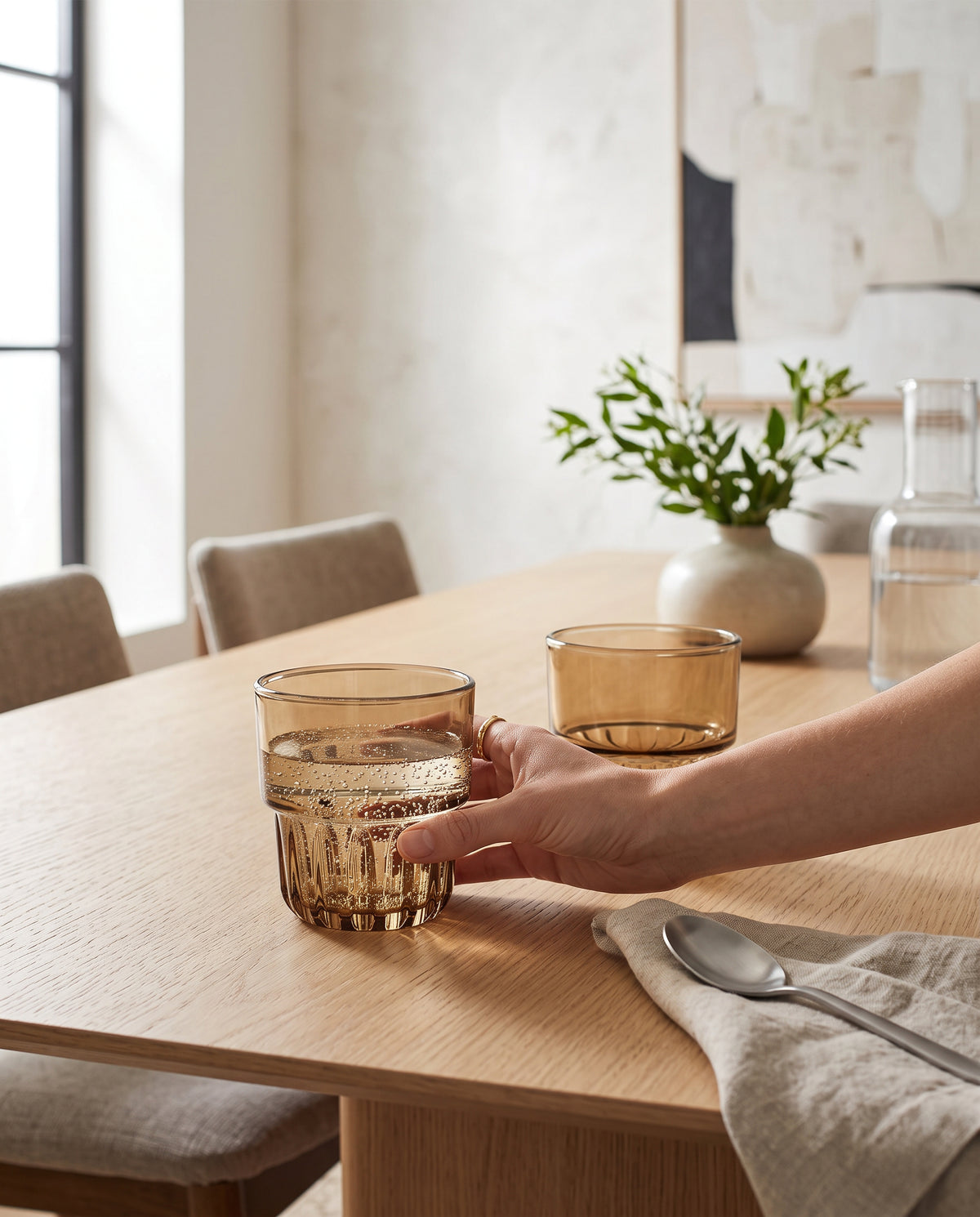 Brown water glasses on a wooden dining table, a hand reaching for one