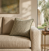 Green piped printed cushion on a beige sofa in a sunlit room