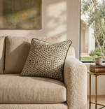 Green piped printed cushion on a beige sofa in a sunlit room