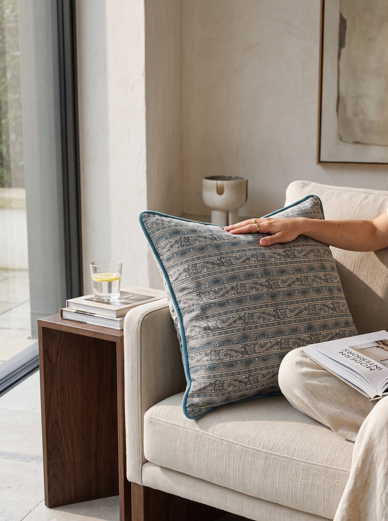 Blue piped printed cushion on an armchair, a hand resting on it