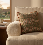 Orange piped cushion with a green zigzag print on a boucle armchair at sunset