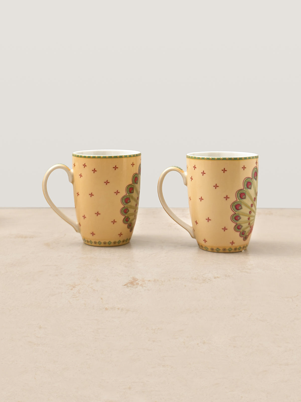 Pair of Mor Bagh Dawn coffee mugs side by side, handles to the left, showing the peacock print