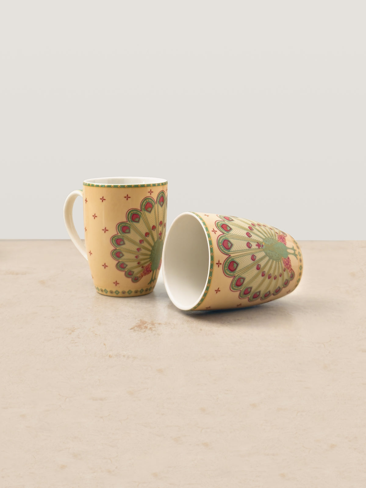 Mor Bagh Dawn coffee mugs, one upright and one on its side, showing the peacock print