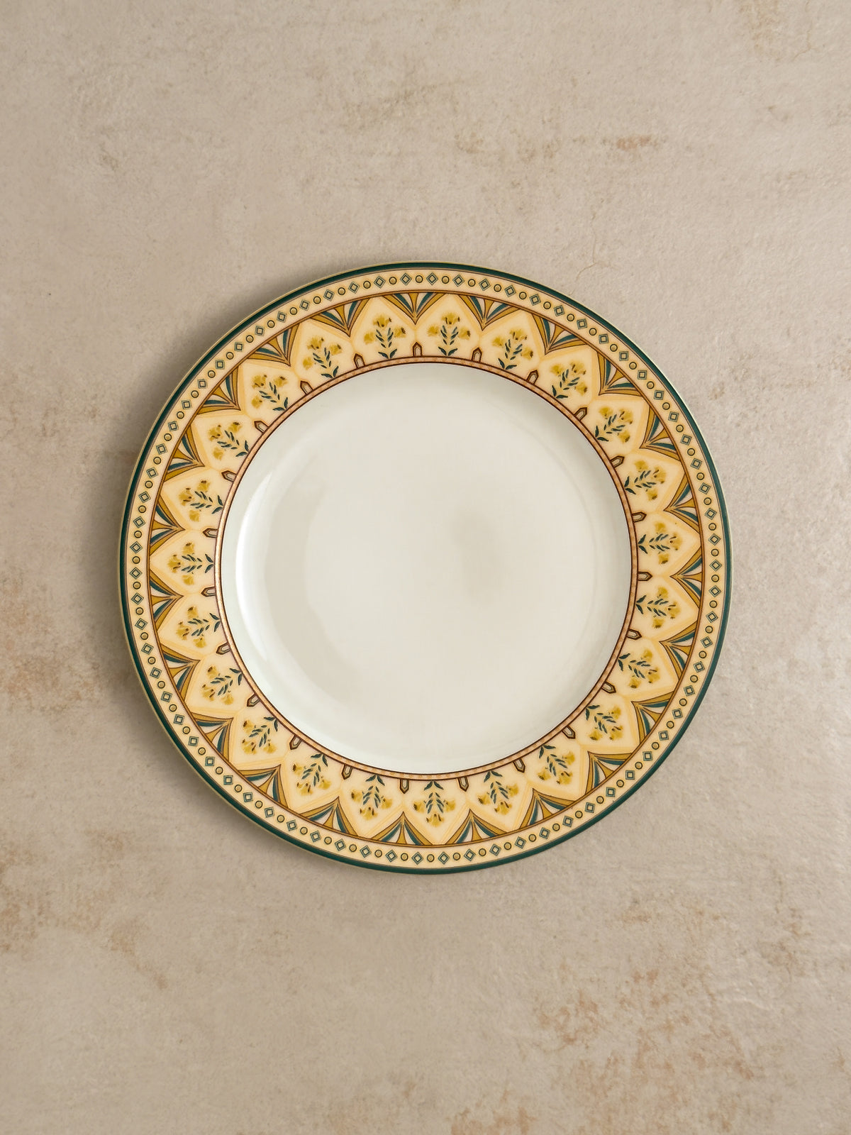 Mor Bagh Dusk dinner plate from above, gold border edged in dark green on a stone background