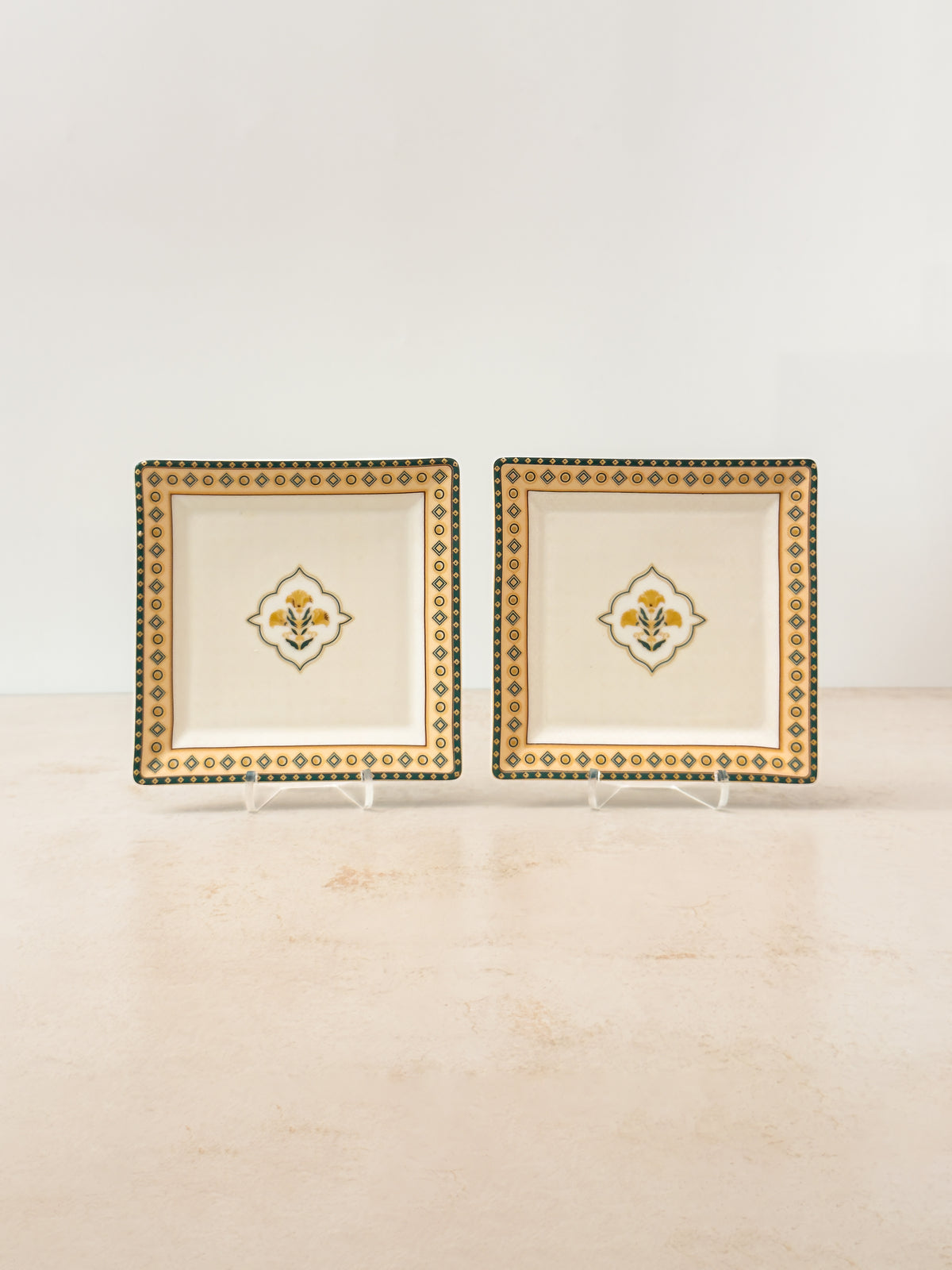 Two Mor Bagh Dusk porcelain square platters on stands with a gold border and centre motif