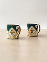 Two Mor Bagh porcelain tea mugs in Dusk, deep green with a cream lotus panel, front view