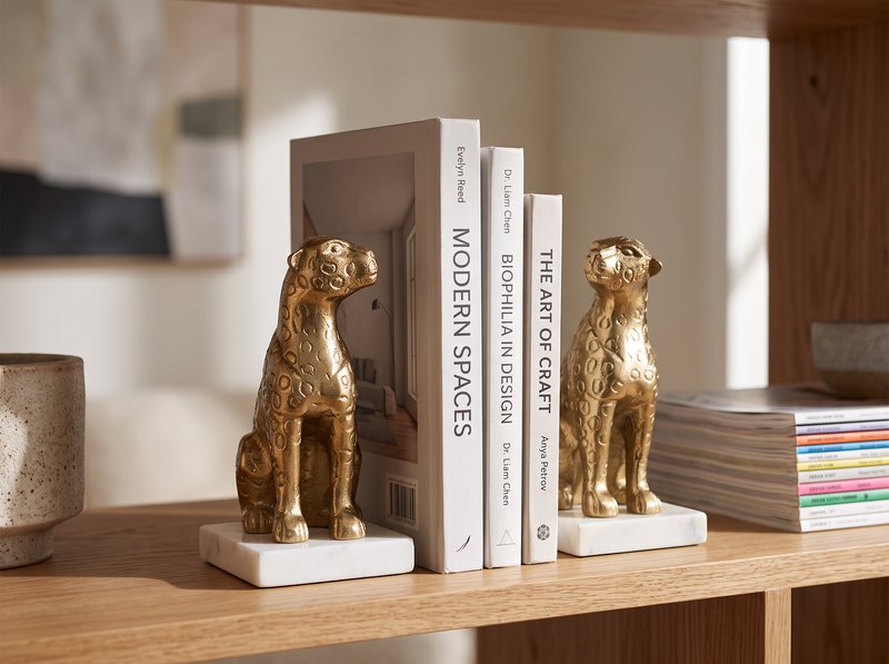 Gold leopard bookends on white marble bases holding books on a wooden desk