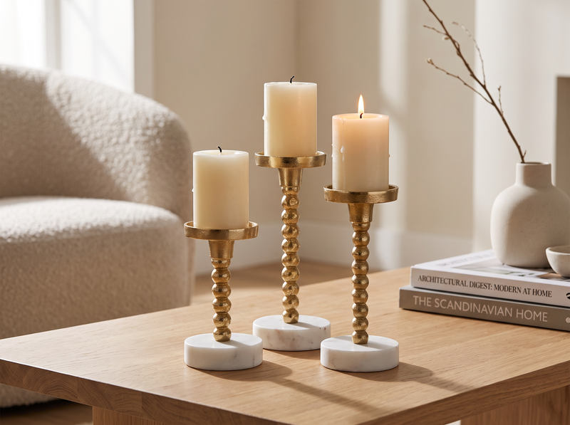 Gold marble candle holders in three heights with lit pillar candles on a wooden coffee table