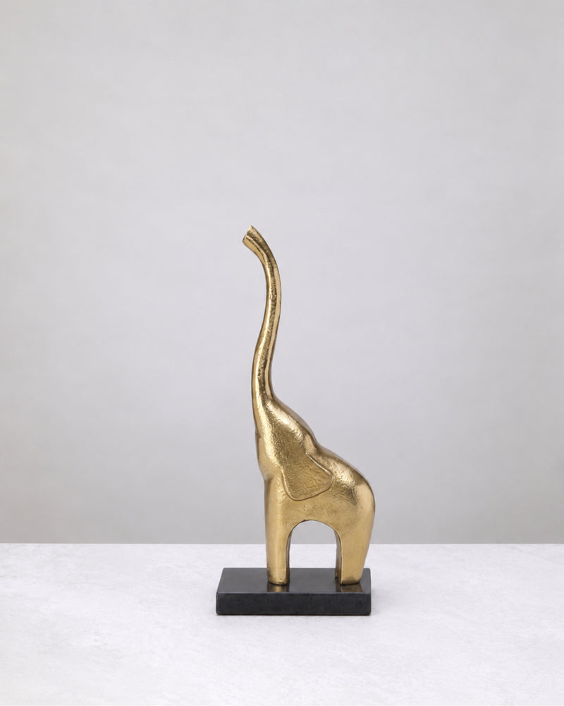 Slim gold elephant with its trunk raised high, standing on a black marble base