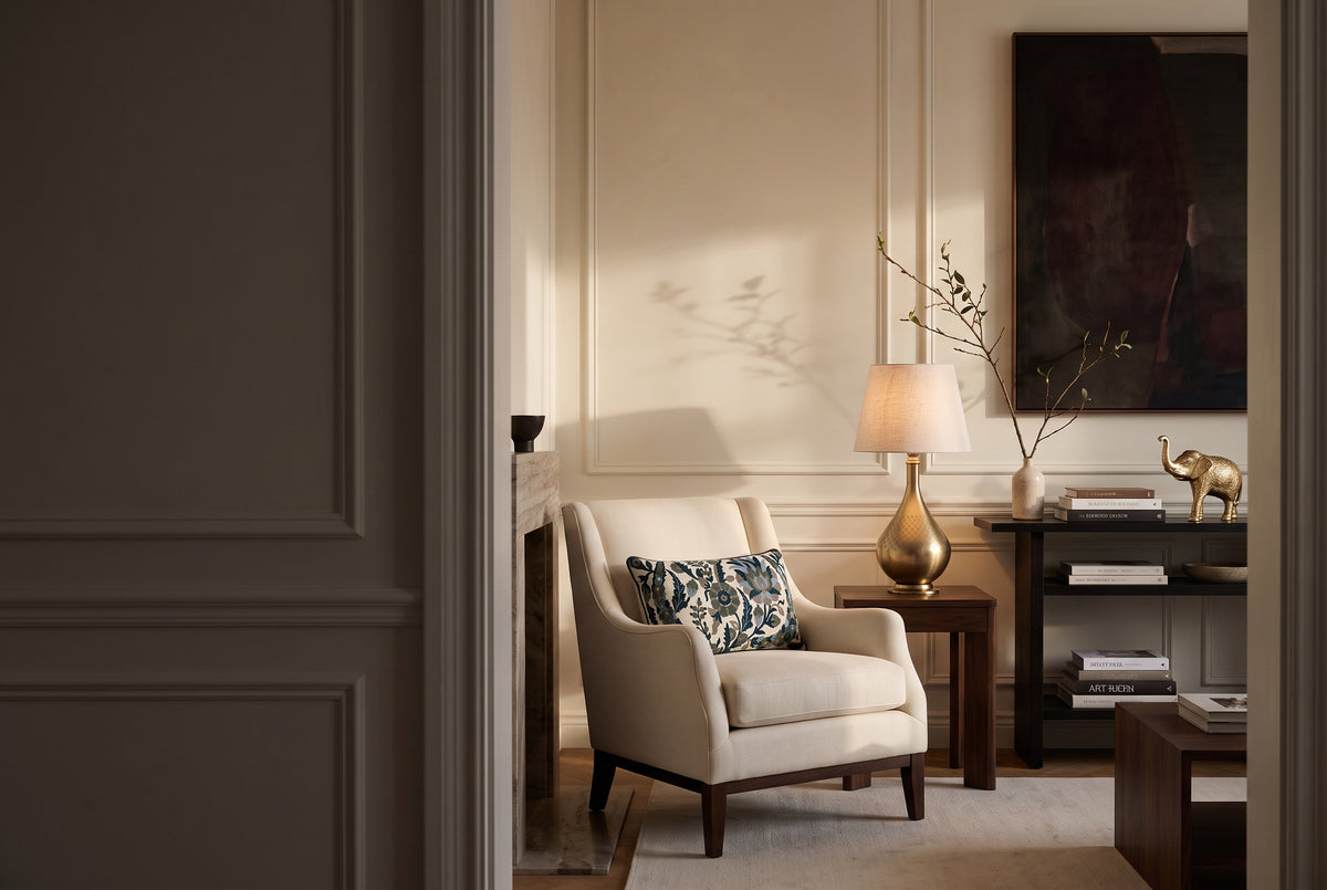 Tufted accent linen pillow on a cream armchair beside a glowing brass lamp in a panelled living room