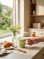 Sage green Blossom ceramic mug on a kitchen counter beside croissants and a jar of flowers