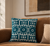 Teal Ari cushion on a tan leather sofa beneath abstract art