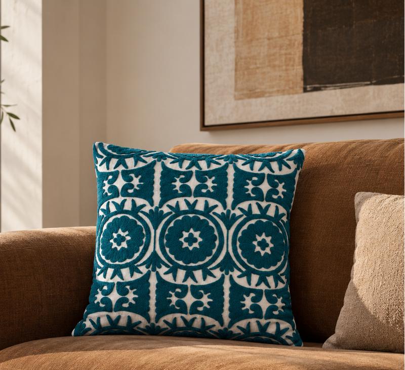 Teal Ari cushion on a tan leather sofa beneath abstract art