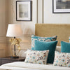 Off white tufted linen pillows with teal cushions on a bed beside a lamp
