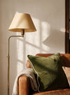 Olive green piped velvet cushion on an armchair beside a floor lamp