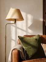 Olive green piped velvet cushion on an armchair beside a floor lamp