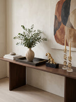 Champagne faceted crystal candle holders on a dark wood console beside a vase of greenery and a gold lion figure