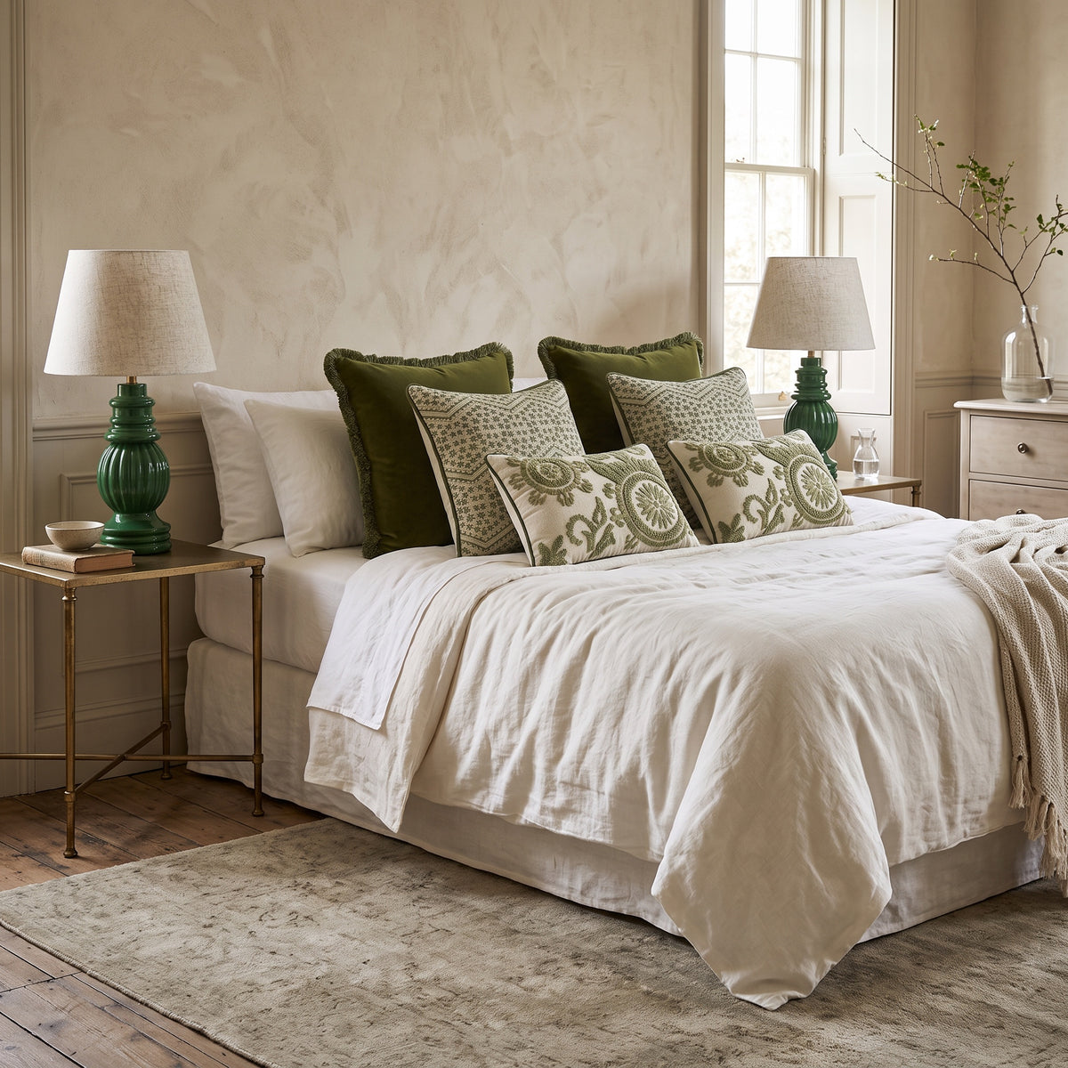 Green printed cushions layered on a white bed with green bedside lamps