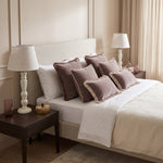 Dusty pink frill velvet lumbar cushions on a white bed between two bedside lamps
