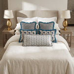 Blue flange and printed cushions layered on a bed between brass bedside lamps
