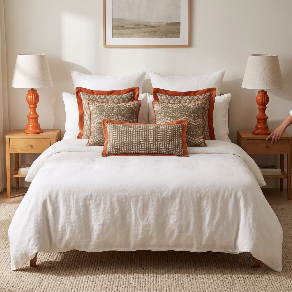 Orange flange and printed cushions on a white bed between coral bedside lamps