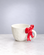 White textured ceramic mug with a cherry red ribbon bow handle