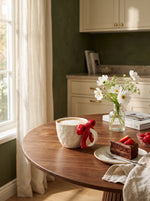 Cherry red Ribbon Bow ceramic mug on a round wooden table with cake and white flowers