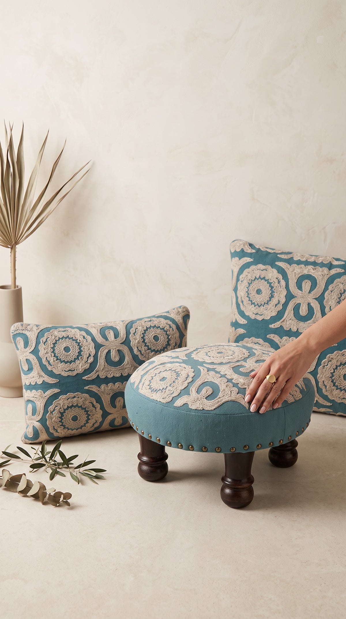 Teal Dori cushion and pillow beside a matching round foot stool, a hand on the stool