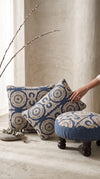 Blue Dori round foot stool beside matching cushions, a hand placing a cushion