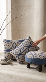 Blue Dori round foot stool beside matching cushions, a hand placing a cushion
